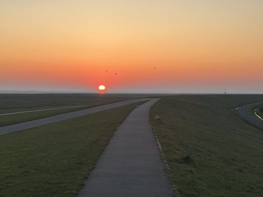 Sonnenaufgang auf dem Deich Friedrichskoog-Spitze atemberaubend, mit leuchtend orangem Himmel, unweit Ferienhaus Huus Marie